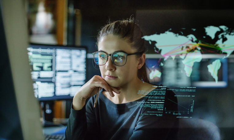 Woman wearing glasses surrounded by computer screens