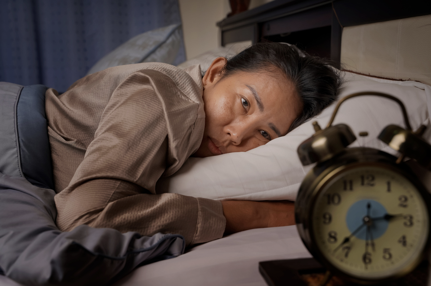 Woman lies awake in bed looking at clock